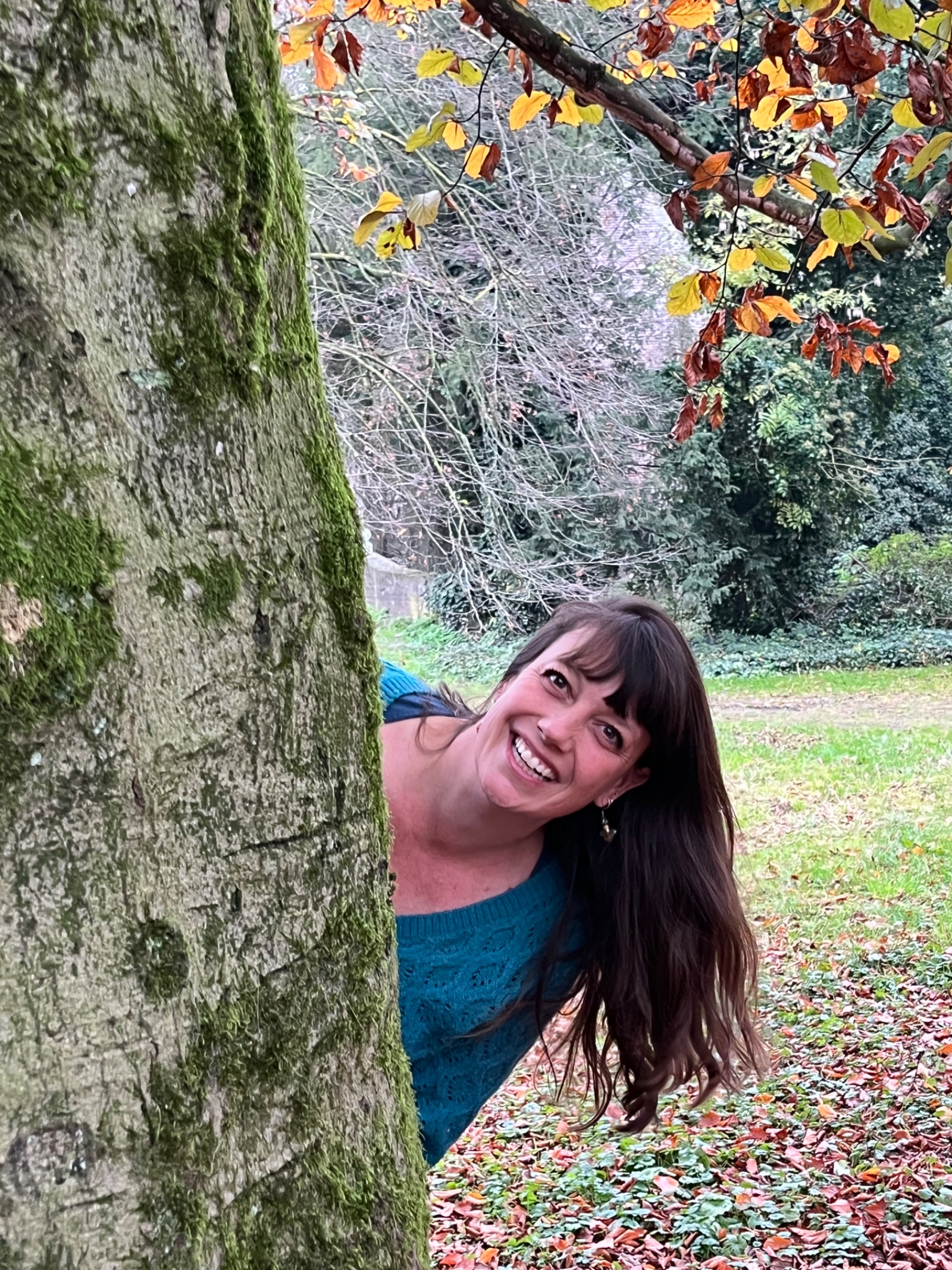 Noor lacht, leunend om een bemoste boomstam in een herfstig park
