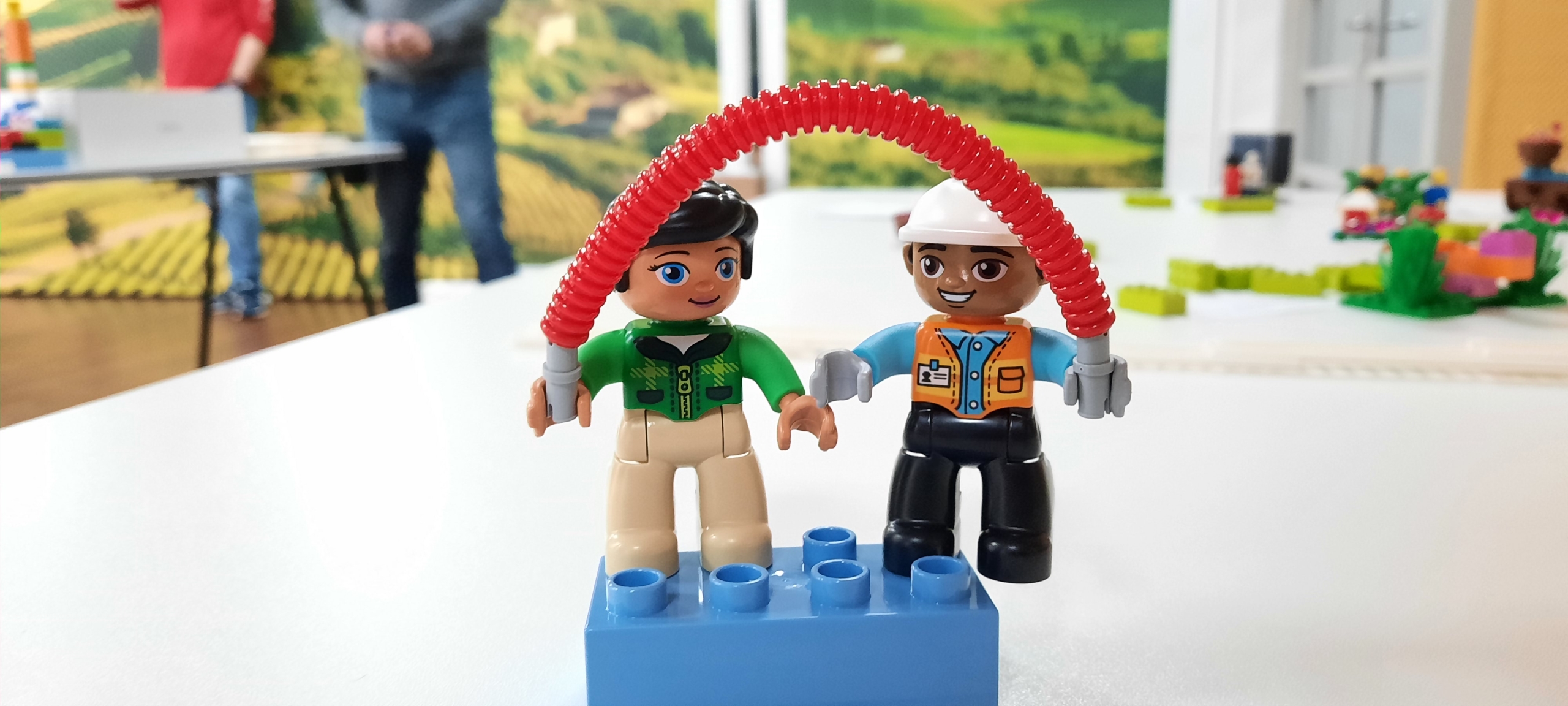 Twee poppetjes van bouwsteentjes, verbonden door een rode boog, gebouwd tijdens een teamdag